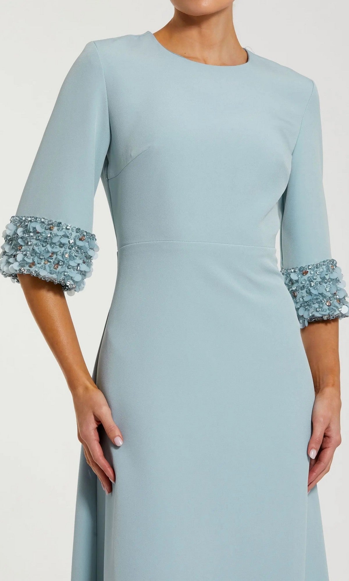 A woman is wearing the Mac Duggal 2342 long formal dress in light blue, featuring modest elbow-length sleeves, elegant beaded cuffs, and 3D floral embellishments.